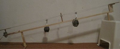 Gesamtansicht mit Umlauf- und Stützrollen auf einem Holzunterbau. Das Seil ist ein 0,8 mm Stahseilmit Kunststoffummantelung und herkömmlicher Quetschklemme verbunden.