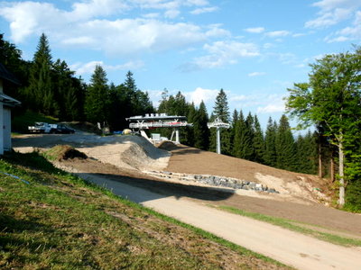 Hier ist die Piste von der Bergstation der Zubringerbahn (in der Bildmitte) zur Iselerbahn zu sehen. Links (grau) die schon bisher vorhandene rote Piste "Waldschneise", die von der Iselerbahn runterkommt. Rechts (braun) die neu angelegte blaue Piste zum bisherigen Zubringerhang. Die beiden Pisten werden wohl im Winter durch mobile Schneezäune abgetrennt. Der hier zu sehende Übergang über den Bach ist etwa doppelt so breit wie früher.