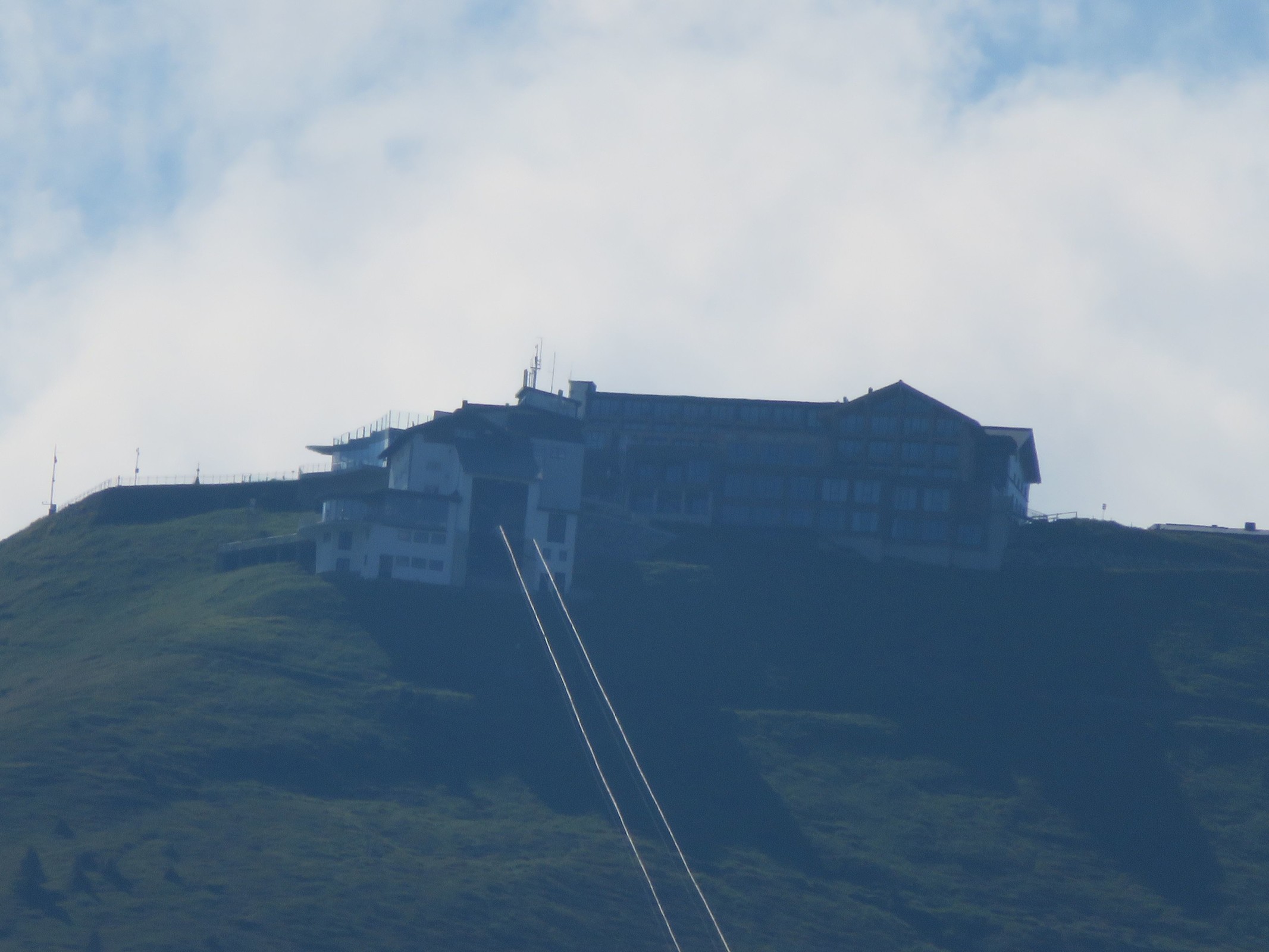 Zoom zum Gipfel der Schmittenhöhe. Hier ist der SchnapsHans, das Berghotel Schmittenhöhe und die Bergstation der 1927 erbauten Schmittenhöhebahn zu sehen.