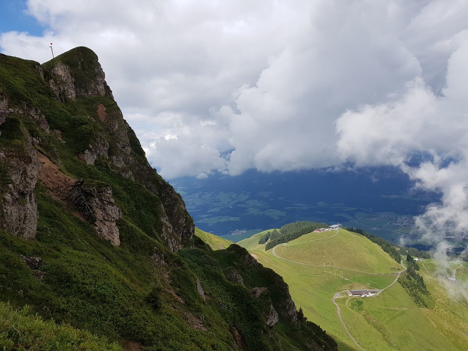 Hinter den Wolken verbirgt sich der Wilde Kaiser. Rechts in der Sonne liegt die Bergstation der Harschbichlbahn.