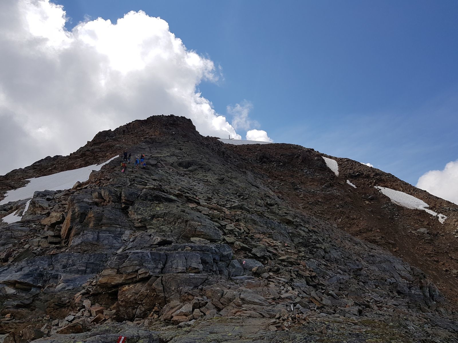 Das Gipfelkreuz lugt bereits hervor, aber man sollte sich nicht stressen, denn ein falscher Schritt kann bereits ein Schritt zu viel sein. Ich versteh eh nicht, wie sich die ganzen Berge noch zusammenhalten, da sie quasi nur aus Geröll bestehen.