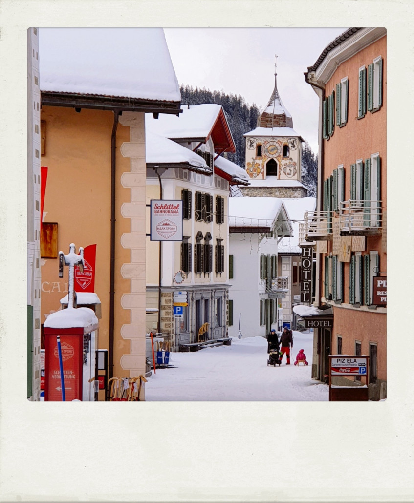 Blick die Hauptstraße hinab. Ein bisschen fühlt es sich an wie früher im Schwarzwald, als man die Kinder ebenfalls mit dem Schlitten noch durchs Dorf zog. Dieser Anblick ist dank Klimaerwärmung zumindest in den Tälern selten geworden. Umso schöner, dass hier noch ein "richtiger" Winter herrscht. Der Turm im Hintergrund ist übrigens kein Kirchturm, sondern eine Art Wehrturm, uralt! Wenn ich recht erinnere, 12. Jahrhundert.
