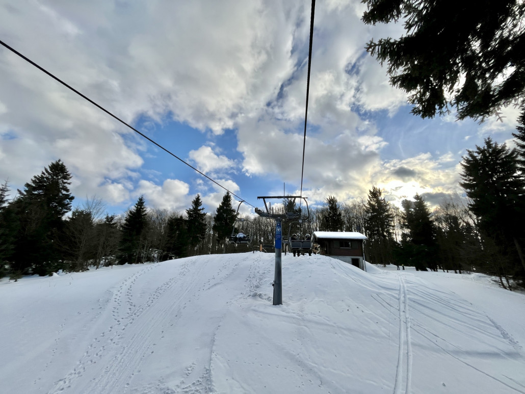 Bergstation in Sicht, rechts in den Wald bei den beiden Skifahrern zweigt die blaue Piste ab, die 180° Kurve um das Lifthäuschen herum ist der Start in die rote Abfahrt und links geht’s zur Rodelbahn
