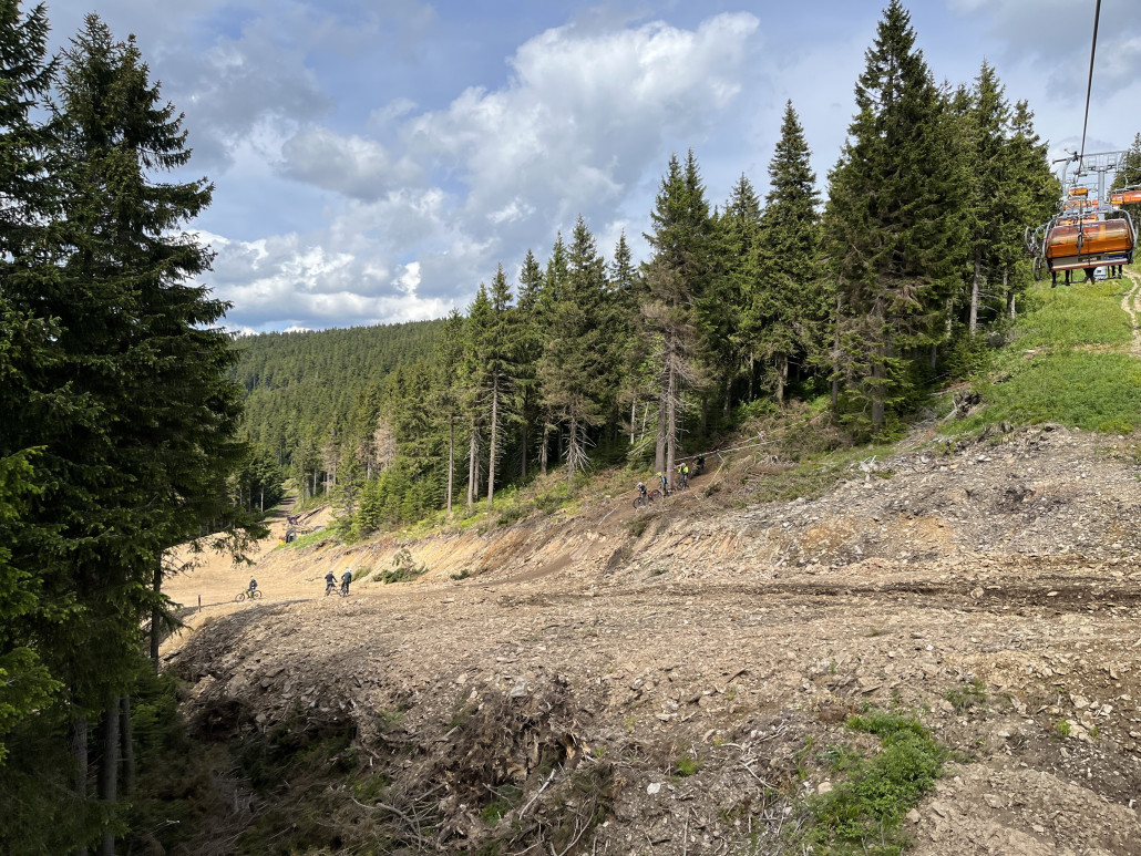 06.06. Ausholzung im Randbereich der Piste ist erfolgt, an der Kehre parken Baufahrzeuge und es wird Holz gelagert