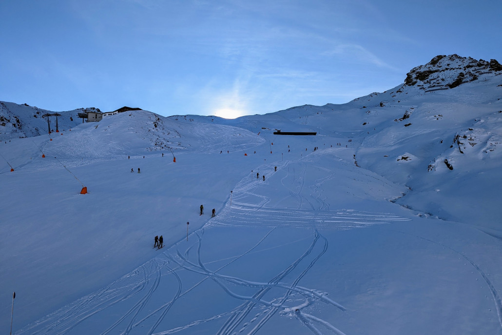 Piste 11, immer noch im Schatten. Man sieht einige Tourengeher den Berg hoch laufen.
