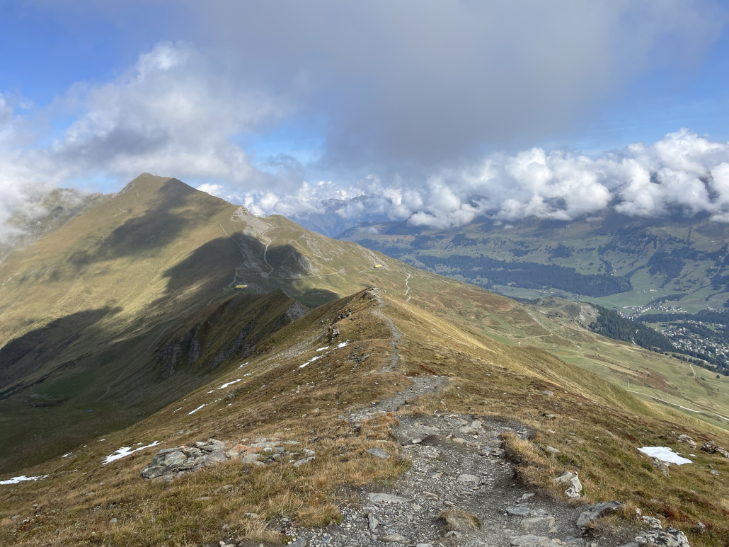 Blick nach Norden im Bereich des Gipfels, der auf 2496m.ü.M. liegt. Die gelben Gebäude sind die Bergstationen der Sesselbahnen Lavoz und Cumacheals. Der aus dieser Perspektive flach aussehende Bergrücken ist das Stätzerhorn, ein weiteres Zwischenziel dieser Wanderung.