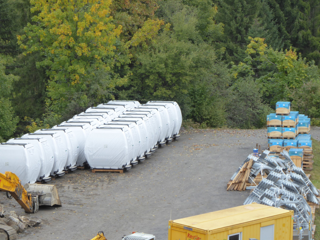 21 Kabinen und das Wartungsgehänge stehen auf dem Parkplatz. In den Kisten mit der blauen Folie befinden sich die Klemmen.