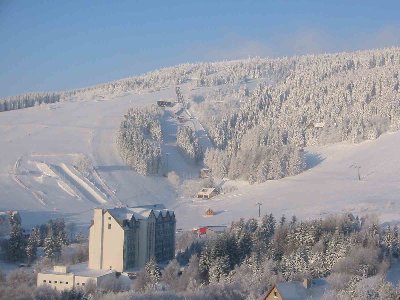Blick zum Kleinen Fichtelberg mit Pisten, Funpark und Schanzenanlage. Im Vordergrund das Hotel &amp;quot;Birkenhof&amp;quot;. Rechts neben den Schanzen im Wald das Hotel Berg-Kristall.