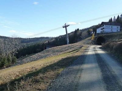 Der erste Abschnitt der neuen Piste. Unmittelbar über der Straße zweigt sie ab, kommt in den Vordergrund und verschwindet links vor der Baumgruppe aus dem Bild.